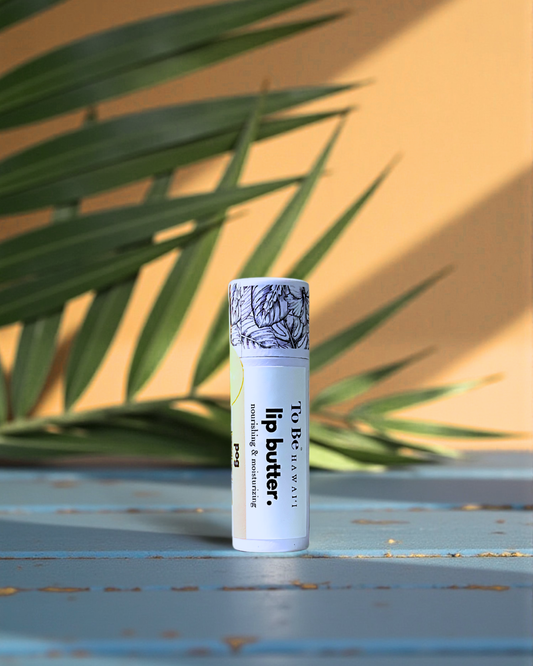 Lip balm tube in the flavor POG with decorative label on a textured surface with green leaves in the background