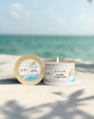 Candle and its packaging on a sandy beach with ocean view